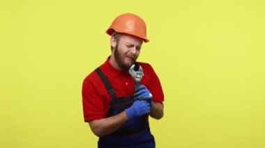 Üzerinde mavi tulum ve turuncu kaskla, mikrofon gibi ayarlanabilir ingiliz anahtarı tutan ve iş sırasında şarkı söyleyen son derece mutlu bir işçi. Sarı arka planda izole edilmiş kapalı stüdyo çekimi.