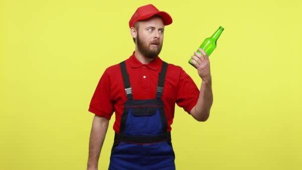 持带有问号的酒瓶纸的可疑杂工 无论是否喝酒 身穿蓝色制服 红色T恤和帽衫 在黄色背景下被隔离的室内拍摄 — 图库视频影像