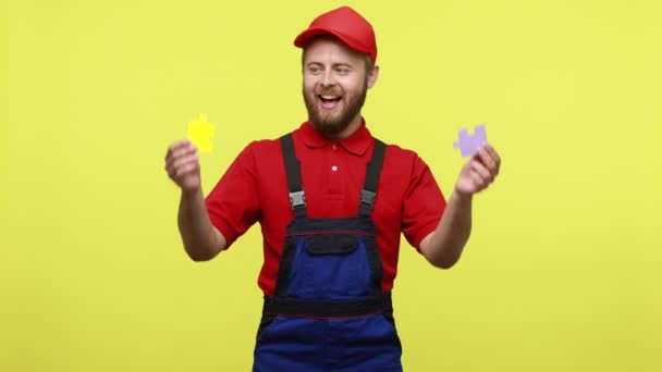 快乐微笑的工人男人连接着两片难题 解决着艰巨的任务 融入社会 穿着蓝色制服 红色T恤和帽衫 在黄色背景下被隔离的室内拍摄 — 图库视频影像