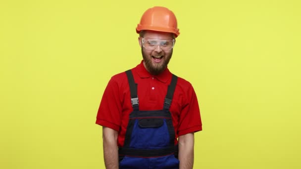 滑稽而乐观的木匠或建筑工人手握锯子 假装在工作 身穿蓝色工作服 头戴橙色头盔 在黄色背景下被隔离的室内拍摄 — 图库视频影像
