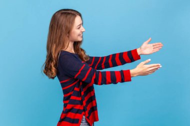 Kollarıma gel! Kazaklı, dost canlısı bir kadın, geniş elleriyle kucaklaşmalar, kucaklaşma, destek ve özen gösterme davetleri. Mavi arka planda kapalı stüdyo çekimi.