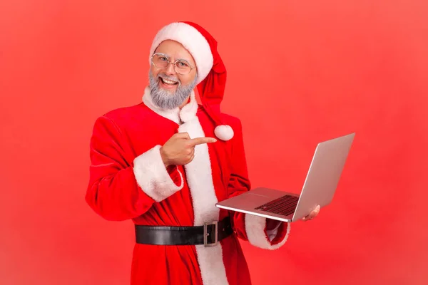 Uśmiechnięty Staruszek Kostiumie Świętego Mikołaja Stojący Laptopem Ręku Pokazujący Ekran — Zdjęcie stockowe