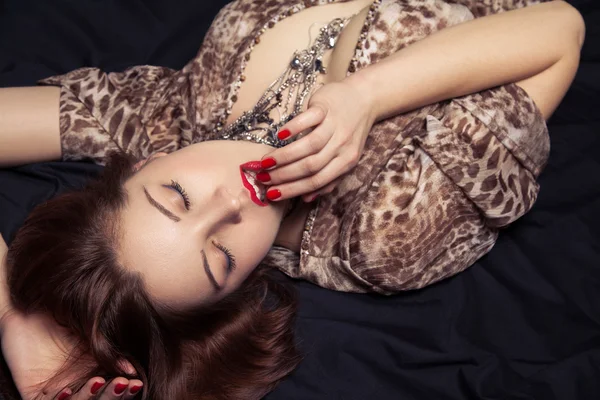 High fashion look. Glamor closeup portrait of beautiful sexy stylish woman model lying on black bed with bright makeup, with red lips, with perfect clean on bed — Stock Photo, Image