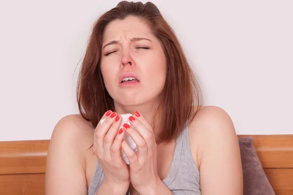 Sneezing beauty. Young sick woman with red nose sitting in bed and sneezing. — Stock Photo, Image