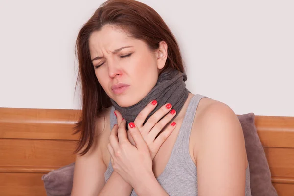 Kranke Frau mit schrecklichen Halsschmerzen. Nahaufnahme einer jungen Frau mit roter Nase im Bett mit dickem Schal, die ihren Hals und Kopf berührt und Schmerzen empfindet — Stockfoto