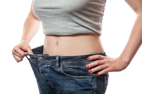 Primo piano della vita sottile della giovane donna in jeans grandi che mostrano una perdita di peso di successo, isolata su sfondo bianco, concetto di dieta — Foto Stock