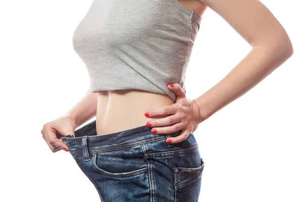 Primo piano della vita sottile della giovane donna in jeans grandi che mostrano una perdita di peso di successo, isolata su sfondo bianco, concetto di dieta — Foto Stock