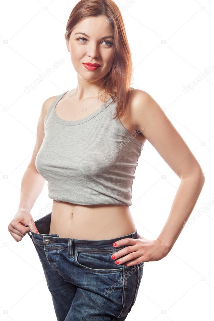 Full-length portrait of attractive slim european young smiling woman in big jeans showing successful weight loss with her happy face, isolated on white background