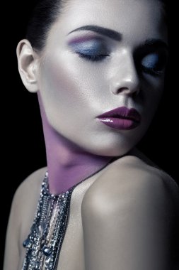 Different style of beauty. young beautiful fashion model with silver, purple, blue makeup and shiny silver jewelry chain on her face. studio low key shot. retouched with special care and attention.