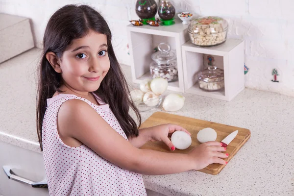 Hermosa niña de 7 años del medio oriente está trabajando con cuchillo y cebolla en la cocina blanca . —  Fotos de Stock