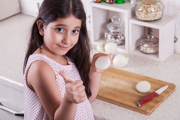 Hermosa niña de 7 años del medio oriente está trabajando con cuchillo y cebolla en la cocina blanca . —  Fotos de Stock