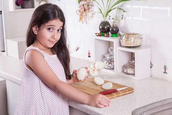 Linda pequena Oriente Médio 7 anos de idade menina está trabalhando com faca e cebola na cozinha branca . — Fotografia de Stock