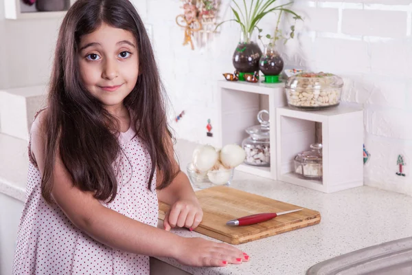 Hermosa niña de 7 años del medio oriente está trabajando con cuchillo y cebolla en la cocina blanca . —  Fotos de Stock