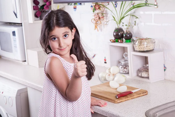 Hermosa niña de 7 años del medio oriente está trabajando con cuchillo y cebolla en la cocina blanca . —  Fotos de Stock