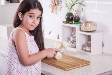 Beautiful little middle eastern 7 years old girl is working with knife and onion in the white kitchen.