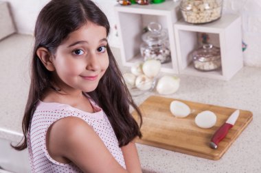 Beautiful little middle eastern 7 years old girl is working with knife and onion in the white kitchen.