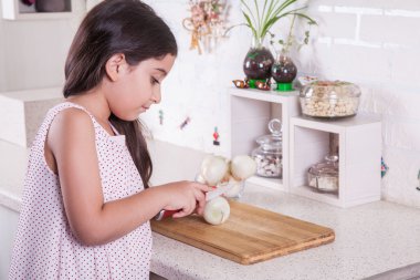 Beautiful little middle eastern 7 years old girl is working with knife and onion in the white kitchen.