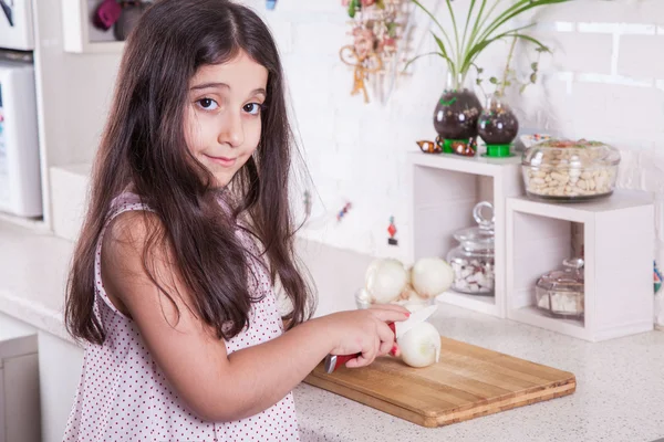 Linda pequena Oriente Médio 7 anos de idade menina está trabalhando com faca e cebola na cozinha branca . — Fotografia de Stock