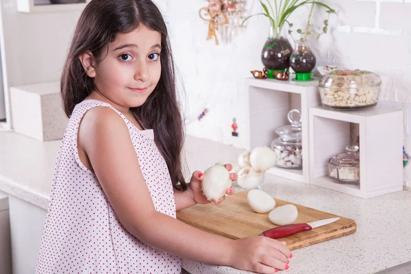 Hermosa niña de 7 años del medio oriente está trabajando con cuchillo y cebolla en la cocina blanca . —  Fotos de Stock