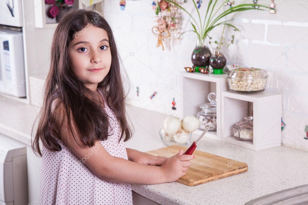 Beautiful little middle eastern 7 years old girl is working with knife and onion in the white kitchen.