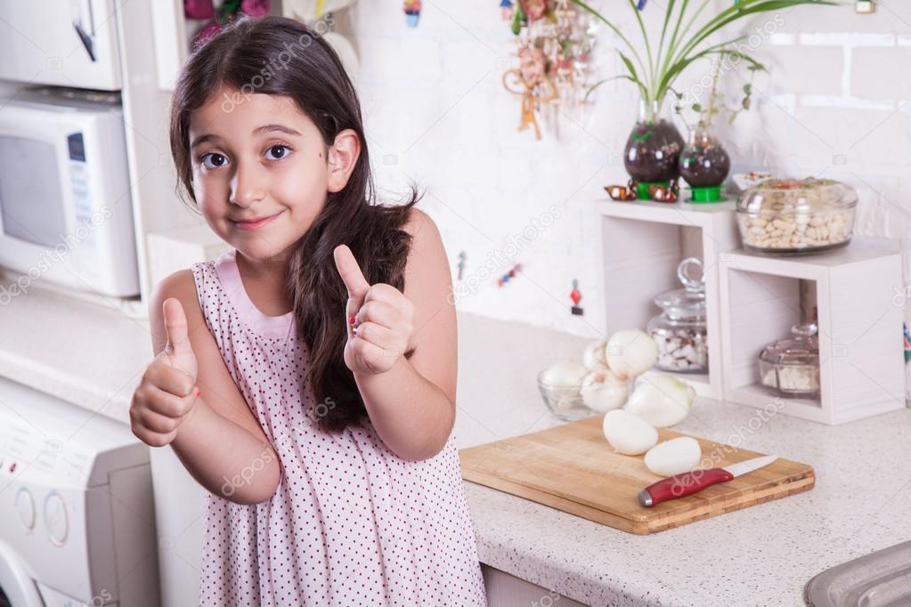 Beautiful little middle eastern 7 years old girl is working with knife and onion in the white kitchen.