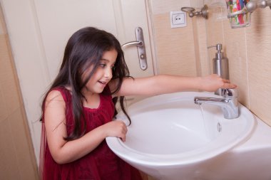 one beautiful little middle eastern arab girl with red dress is washing her hands clipart