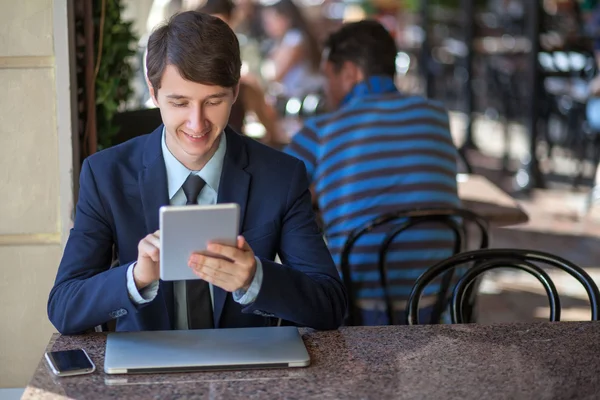 One relaxed young handsome professional businessman working with his laptop, phone and tablet in a noisy cafe. — Stock Photo, Image