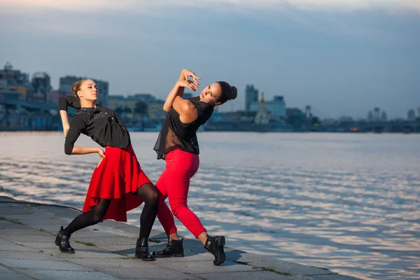 Two young beautiful twin sisters are dancing waacking dance in the city background near river.