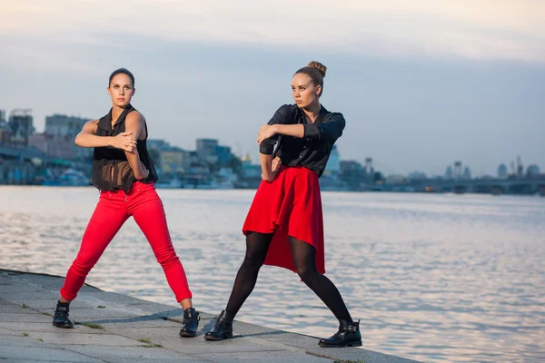 Duas irmãs gêmeas bonitas jovens estão dançando dança waacking no fundo da cidade perto do rio . — Fotografia de Stock