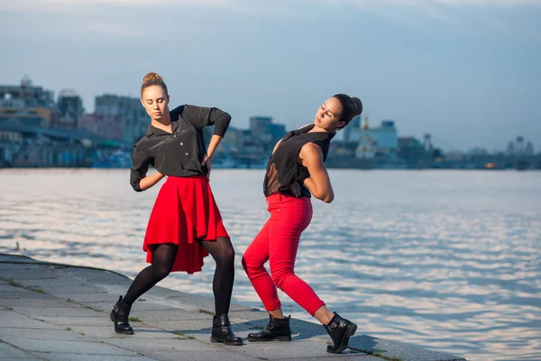 Duas irmãs gêmeas bonitas jovens estão dançando dança waacking no fundo da cidade perto do rio . — Fotografia de Stock