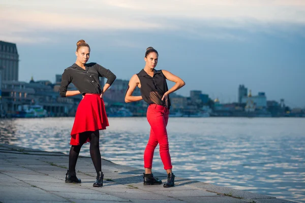 Dos hermanas gemelas hermosas jóvenes están bailando waacking danza en el fondo de la ciudad cerca del río . — Foto de Stock