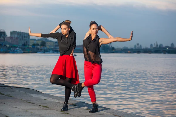 Dvě mladé krásné dvojčata tančí tanec waacking v pozadí města blízko řeky. — Stock fotografie