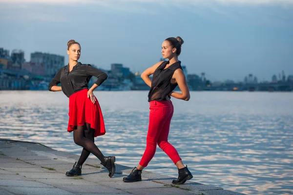 Dos hermanas gemelas hermosas jóvenes están bailando waacking danza en el fondo de la ciudad cerca del río . — Foto de Stock