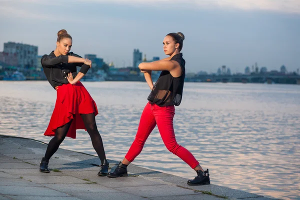 Dos hermanas gemelas hermosas jóvenes están bailando waacking danza en el fondo de la ciudad cerca del río . — Foto de Stock