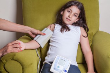 Doctor checking blood pressure of small beautiful middle eastern girl sitting on green chair and feeling bad. clipart