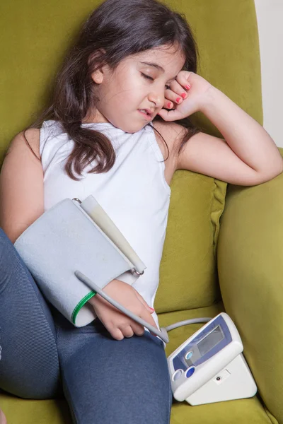 Pequeña chica del medio oriente sintiéndose mal y sosteniendo el dispositivo digital de presión arterial . — Foto de Stock