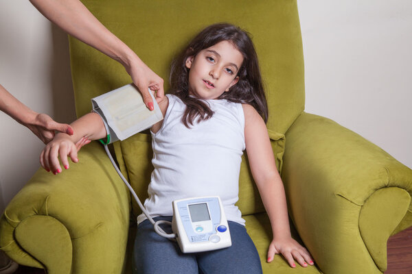Doctor checking blood pressure of small beautiful middle eastern girl sitting on green chair and feeling bad.