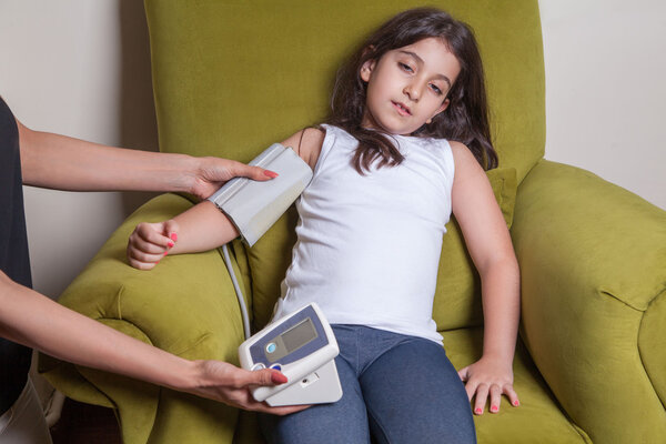 Doctor checking blood pressure of small beautiful middle eastern girl sitting on green chair and feeling bad.