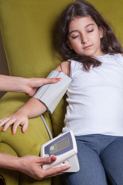 Doctor checking blood pressure of small beautiful middle eastern girl sitting on green chair and feeling bad.