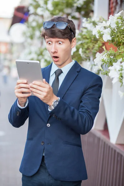 Happy young businessman using and working on tablet PC on a city street, using wireless internet near cafe. — Stock Photo, Image