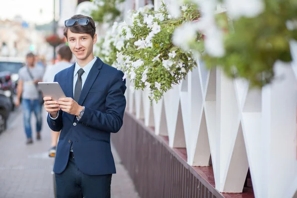 Happy young businessman using and working on tablet PC on a city street, using wireless internet near cafe. — Stock Photo, Image