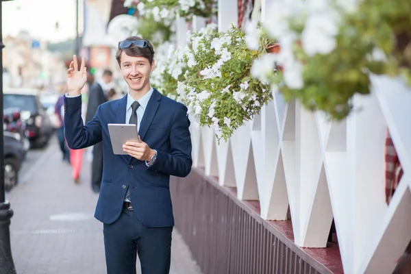 Happy young businessman using and working on tablet PC on a city street, using wireless internet near cafe. — Stock Photo, Image