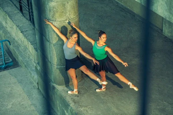 Dos hermanas gemelas jóvenes bailando ballet en la ciudad con traje de ballet. baile de sincronización urbana. Baile callejero industrial. con efecto especial. posando sincronizado. zapatos y vestido de ballet puntiagudo . — Foto de Stock