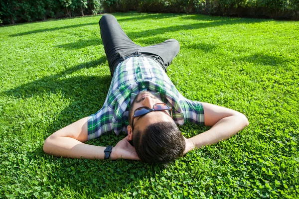 Un uomo medio orientale di moda con la barba, stile di capelli di moda sta riposando su bella erba verde giorno. giovane uomo d'affari arabo 20-30 anni, a riposo dopo un duro lavoro. smartphone, tablet . — Foto Stock