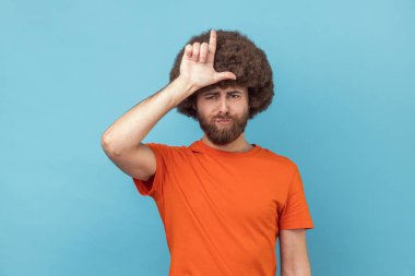 Alnına yakın el ele tutuşmuş depresif bir adamın portresi parmaklarıyla ezik hareketler gösteriyor, sorunları var, mutsuz görünüyor. Mavi arka planda kapalı stüdyo çekimi.