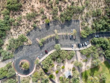 Tucson, Arizona, ABD - 6 Ağustos 2025: Sonoran manzarasında yoğun çöl bitkileriyle çevrili Agua Caliente Bölgesel Parkı 'nın eğimli otoparkının havadan görünüşü