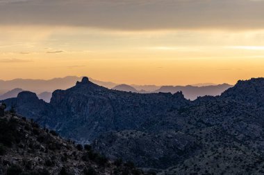 Lemmon Dağı 'ndan dramatik günbatımı manzarası engebeli kayalık tepeler üzerinde altın ışığı uzak dağ sıraları ve bulutlu gökyüzünün altındaki vadiyi gösteriyor.