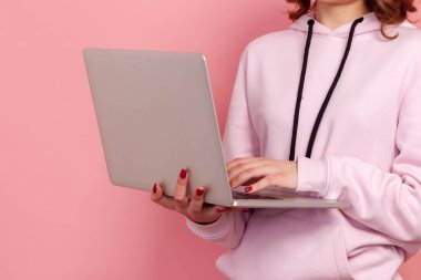 Dizüstü bilgisayar tutan ve klavyede yazan kadının pembe arkaplanda izole edilmiş yakın plan görüntüsü
