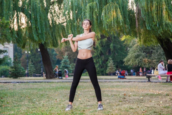 Young happy beautiful sexy girl is stretching in the park garden. people background. with dark hair and black and white sport suit and happiness and smile. on summer or autumn time season. — Φωτογραφία Αρχείου