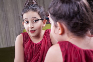 Küçük güzel Arap Ortadoğu kız kırmızı elbise ve dudak makyaj dikkatle evde ayna ile. 8-10 yıl.